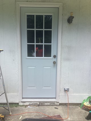A fully installed white exterior door with a glass panel divided into grids, securely fitted into the doorway. The doorframe has been finished with trim.