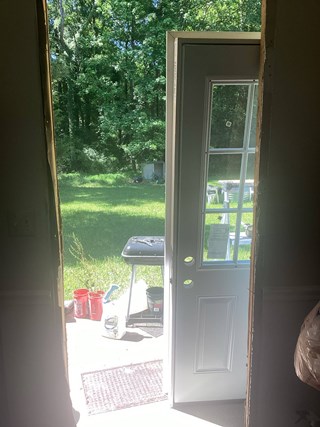 A partially installed white exterior door with a glass panel. The doorframe is exposed with no trim.
