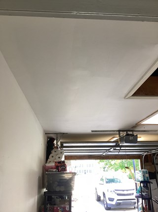 Garage ceiling after repair, now fully covered with smooth drywall. The repaired area blends seamlessly with the rest of the ceiling, which has been freshly painted.