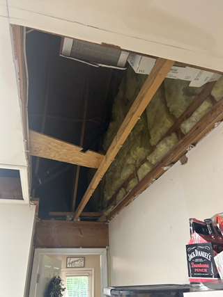 Garage ceiling with a large, exposed section showing wooden beams, insulation, and the roof's interior.
