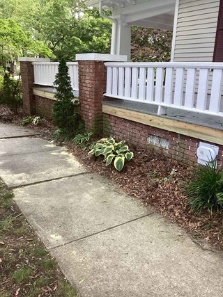 Front porch after repair, featuring a newly replaced fascia board and freshly painted white railing. 
