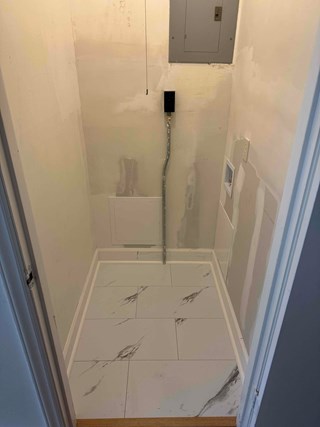Utility closet with newly installed white tiles featuring a marble-like gray veining pattern. The flooring is smooth, clean, and polished, giving the space a modern and fresh look. The walls and baseboards are also updated, complementing the elegant flooring.