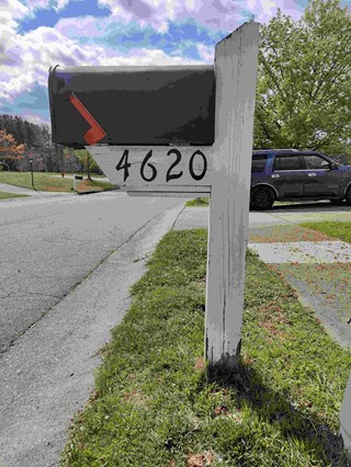 Mailbox post showing a weathered white wooden post that is beginning to rot near the base. 