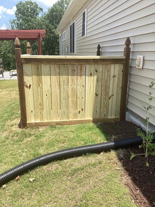  The area where the trash bins are kept has been completely enclosed with a new wooden fence. The fence is taller and solid, with horizontal wooden slats and pointed posts at the top. 
