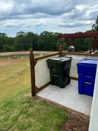 A small fenced area on a patio with a white lattice panel enclosing two trash bins, one green and one blue.