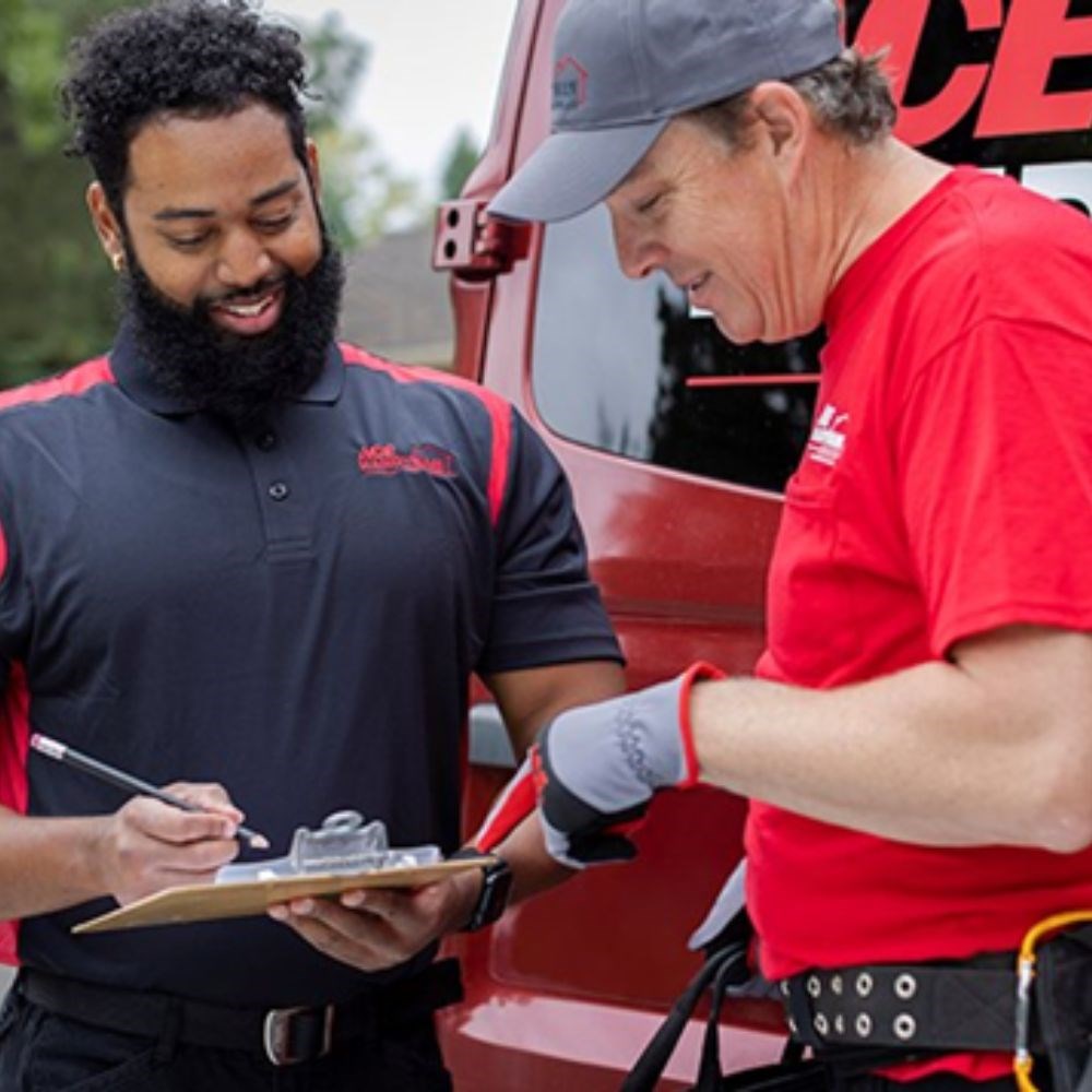 A smiling man in an Ace Handyman Services polo holding a clipboard standing next to a man in an Ace Handyman Services T-shirt pointing at the clipboard. A smiling man in an Ace Handyman Services polo holding a clipboard standing next to a man in an Ace Handyman Services T-shirt pointing at the clipboard.