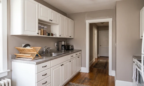 Repaired kitchen with square cabinet doors, patched painted drywall, and a clean dry faucet by the hallway door