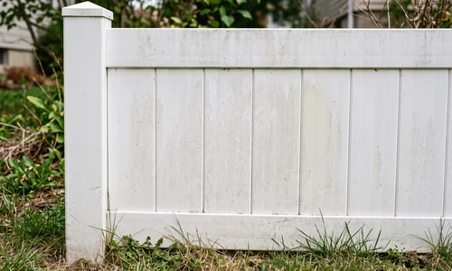 Weathered white vinyl fence panel with chalky oxidation residue and faint discoloration in overcast daylight
