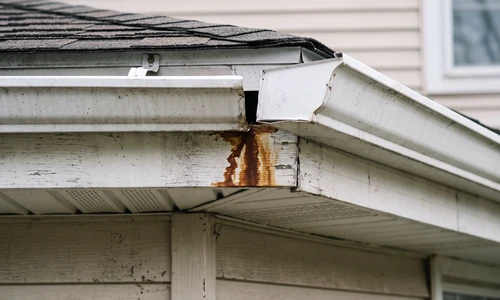 Separated aluminum gutter seam with a rust-brown water stain running down the fascia board below
