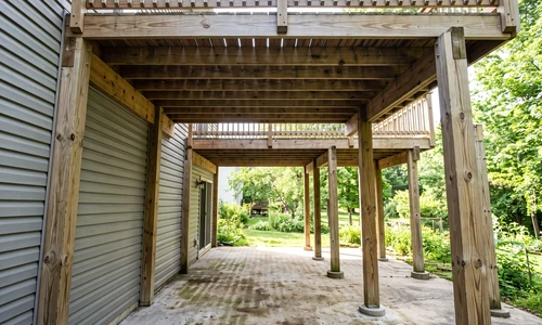 Tall second-storey deck seen from the patio below, with a full storey of headroom and exposed joists overhead