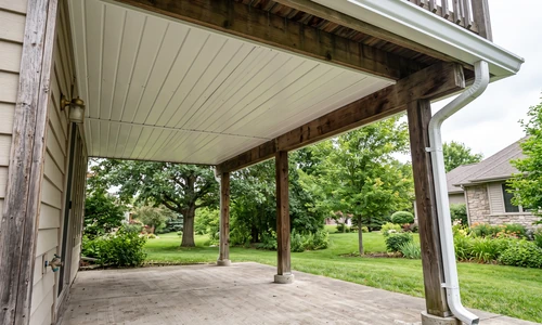 Finished under-deck ceiling with white panels, an integrated gutter trough, and a dry concrete patio below