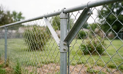 Diagonal braces bolted at forty-five degrees against a chain link fence post, the post standing plumb again