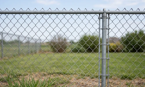 Repaired chain link fence section with new mesh tied into the original fabric, tension bar and ties visible, straight top rail