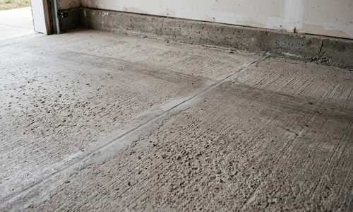 Repaired concrete garage floor with the crack filled flush, leaving a faint seam in the swept slab