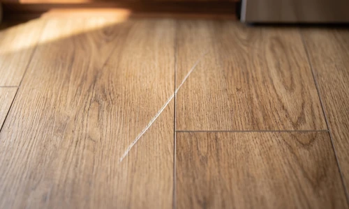 Light scratch running across two vinyl plank boards in a sunlit kitchen, seen from directly above