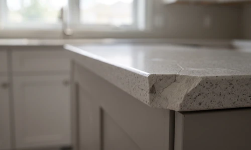 Chipped quartz countertop corner with visible resin damage at the edge, natural kitchen light