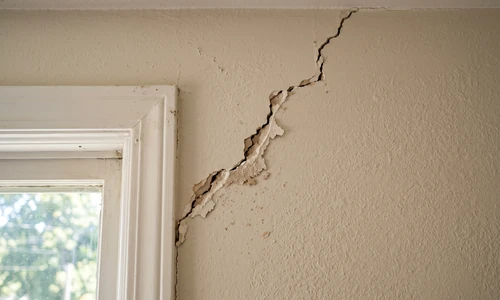 Stair-step diagonal crack running from the corner of a window casing across painted drywall
