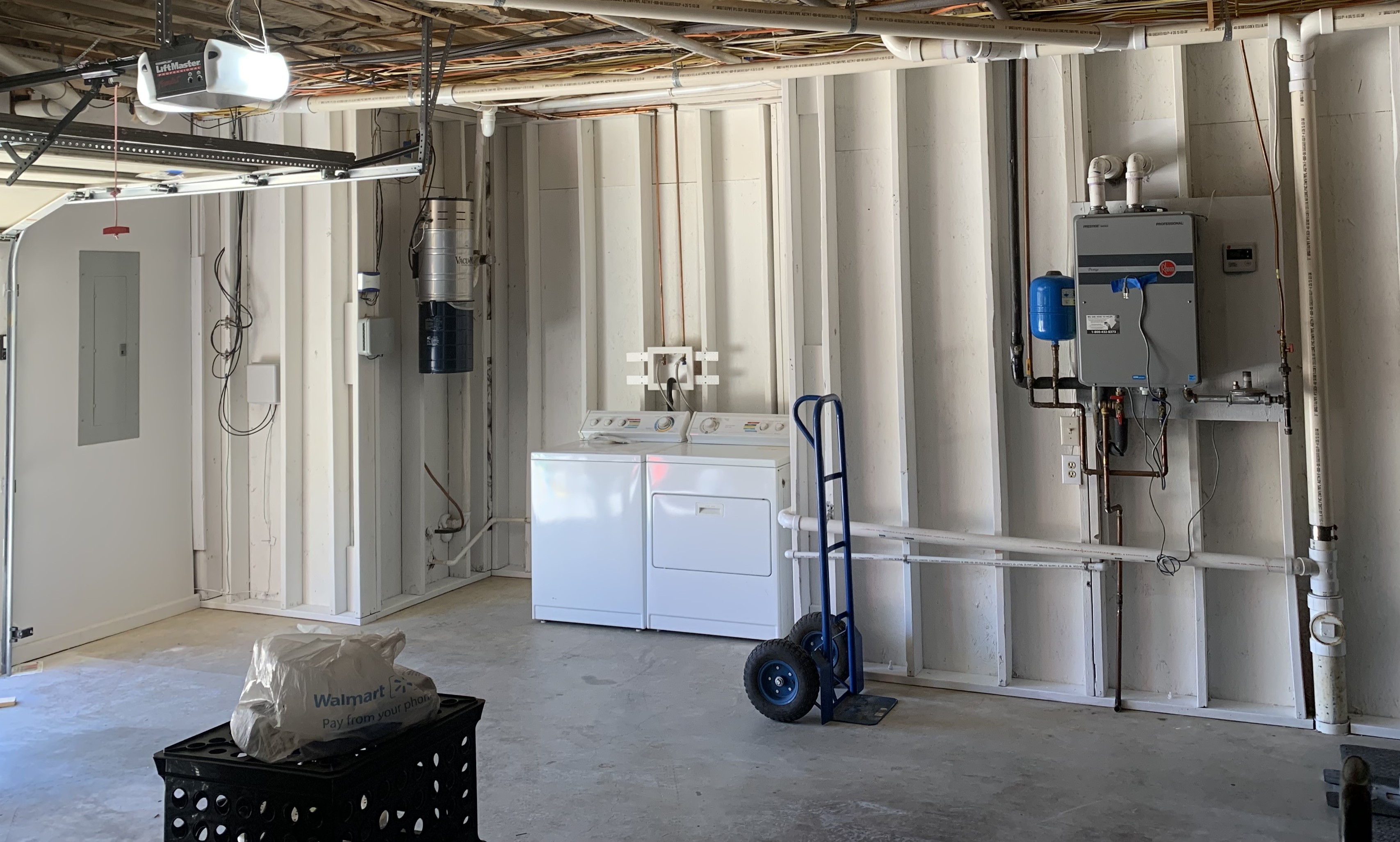 Unfinished utility room with washer, dryer, pipes, and a dolly.