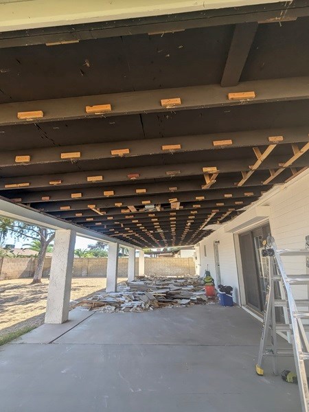 Outdoor ceiling renovation with ladder and scattered tools.