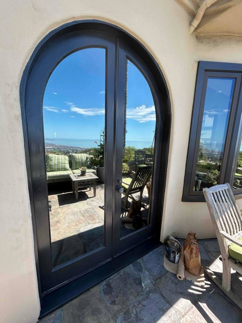 Refinished arched double doors, Huntington Beach Finished arched double doors with a fresh dark finish on a Huntington Beach home, with a patio and ocean view reflected in the glass