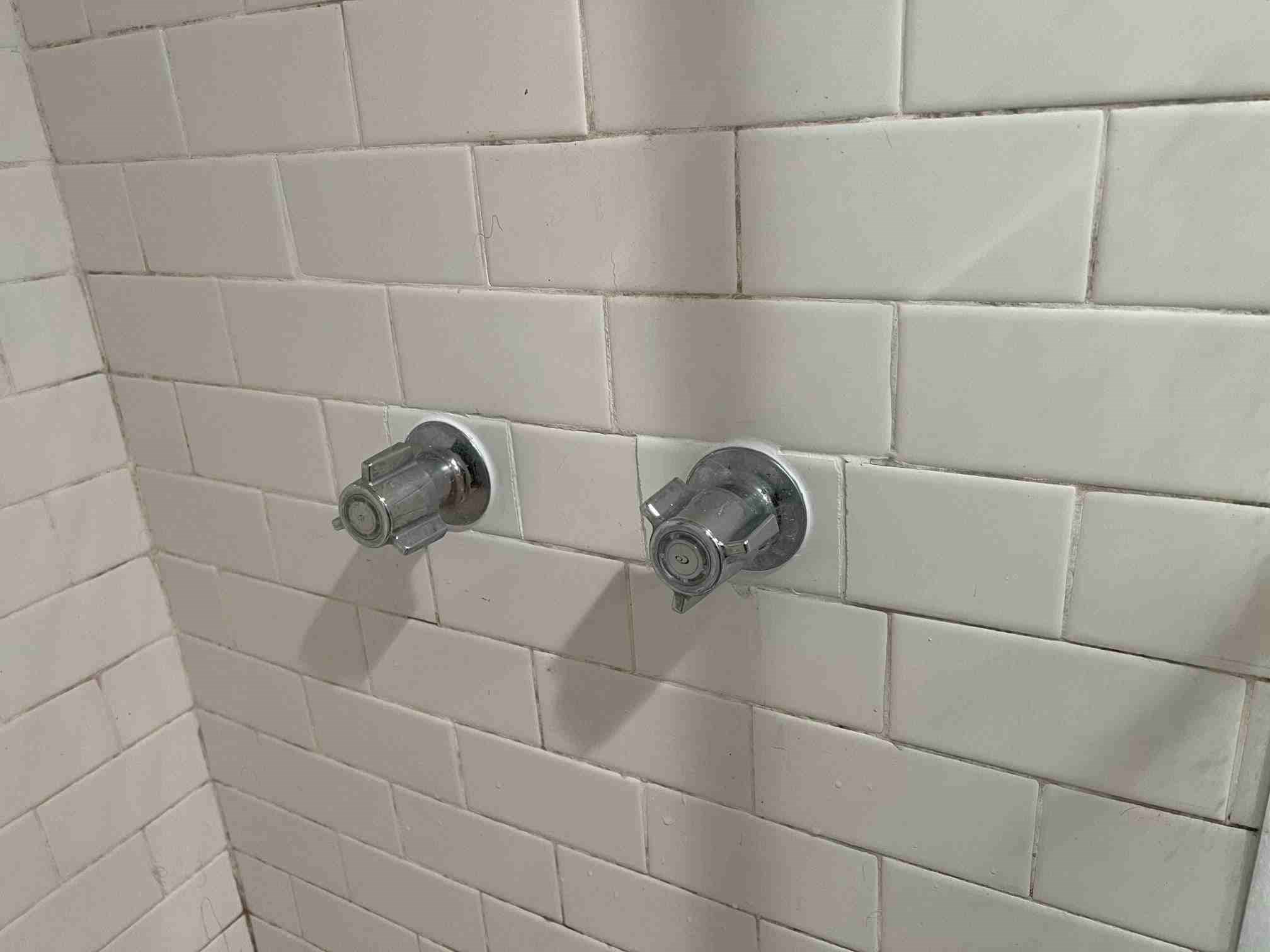 Two chrome faucets on tiled bathroom wall.