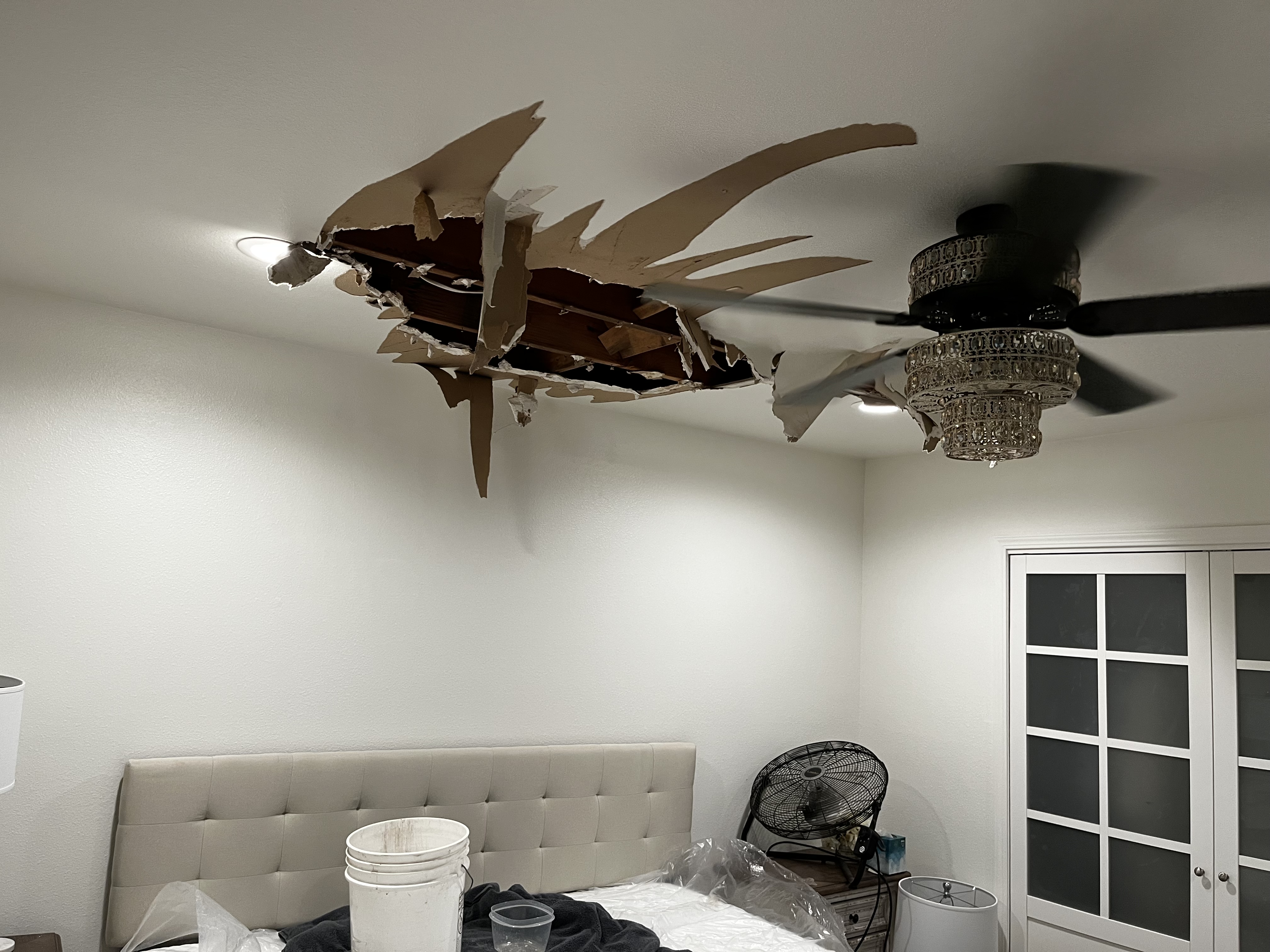 Ceiling damage with exposed beams and debris in a bedroom.