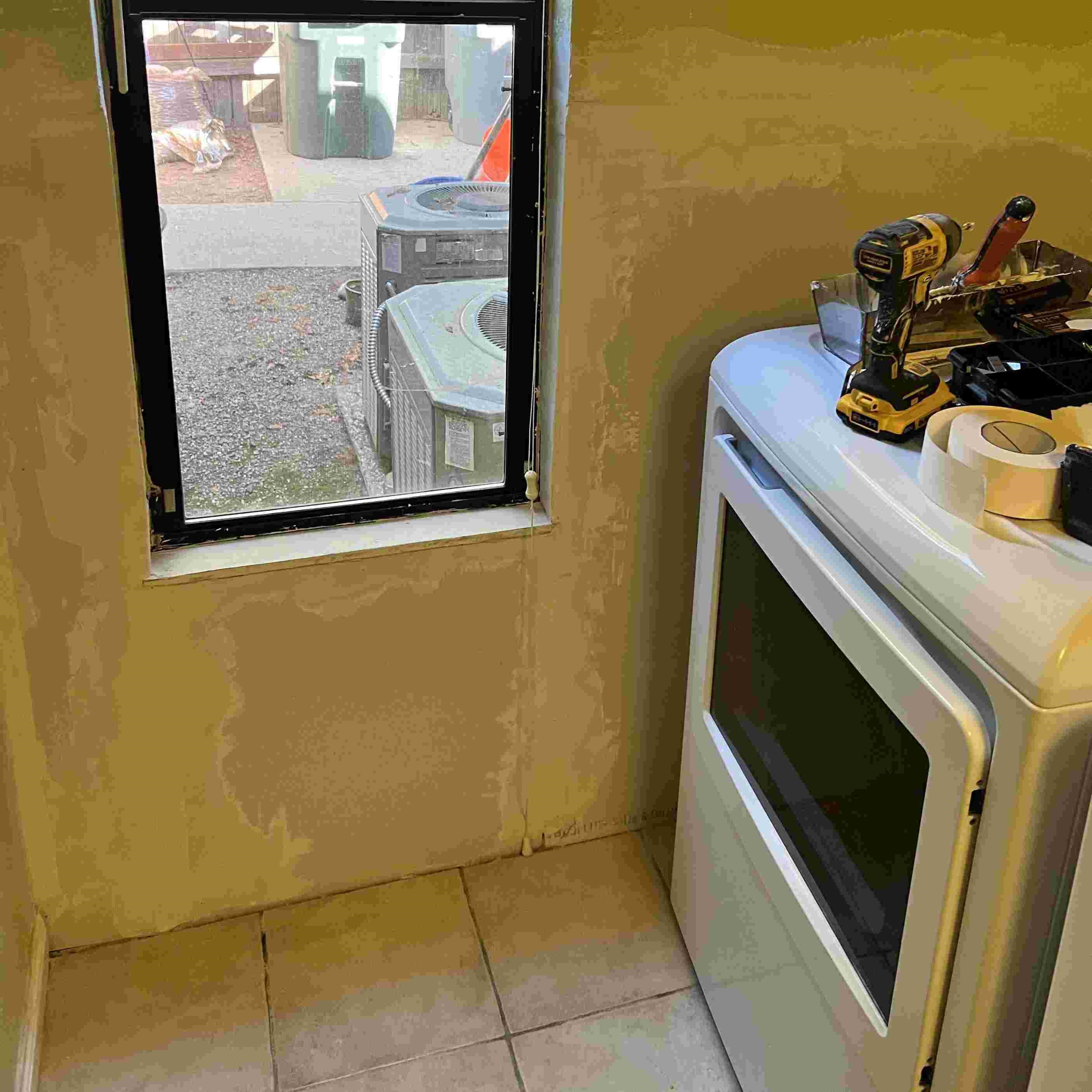 Handyman's tools next to oven by window with unfinished wall.