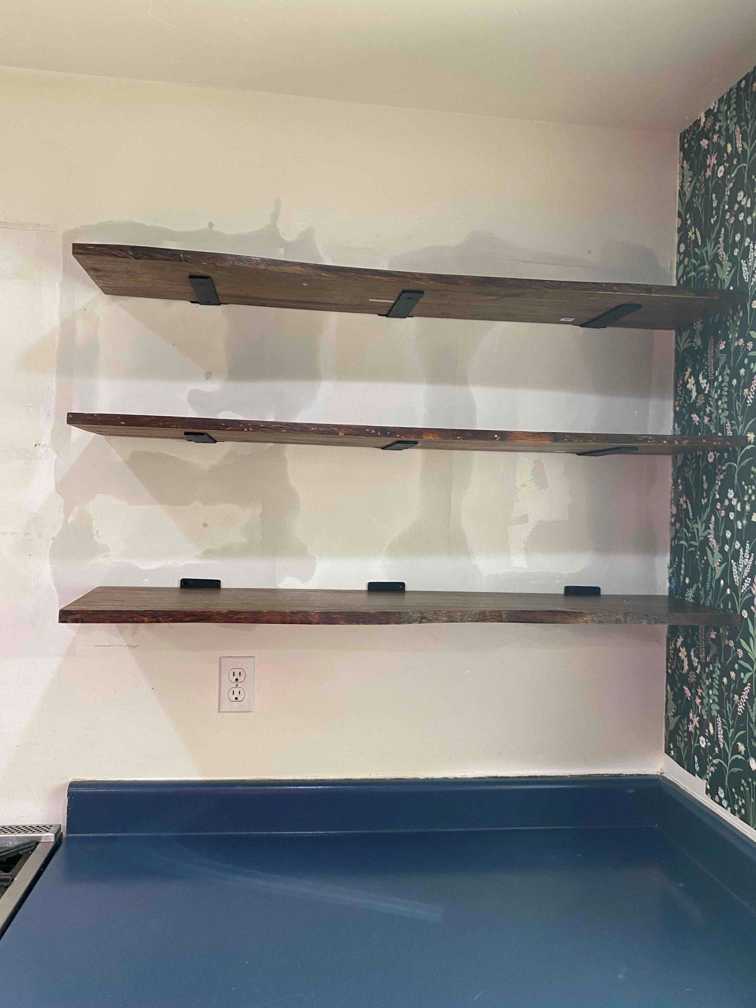 Floating wooden shelves above a counter on a patterned wall.