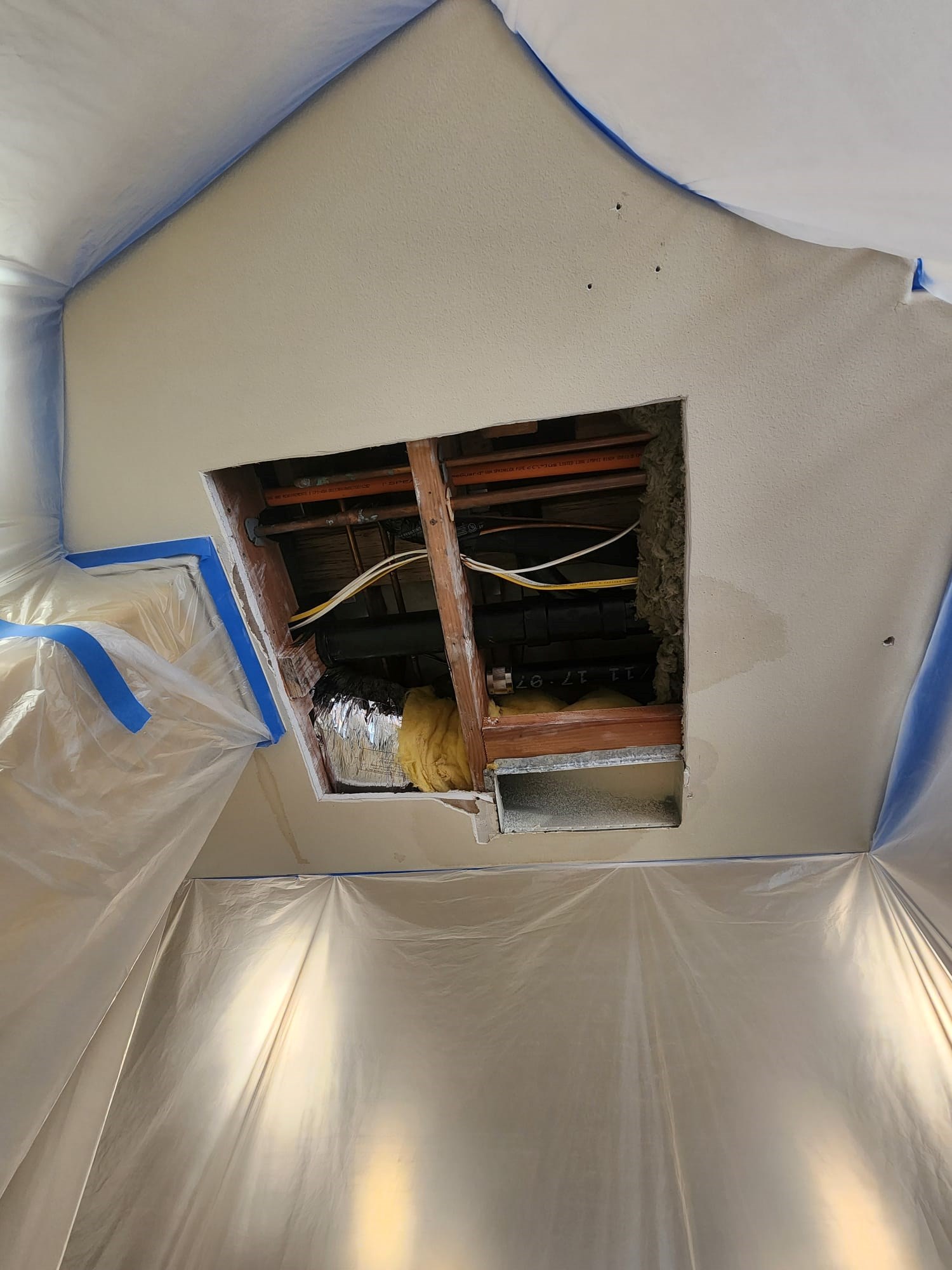 Ceiling with exposed beams and pipes, surrounded by plastic tarp.