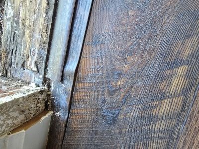 Worn and damaged wooden floor near peeling window frame.
