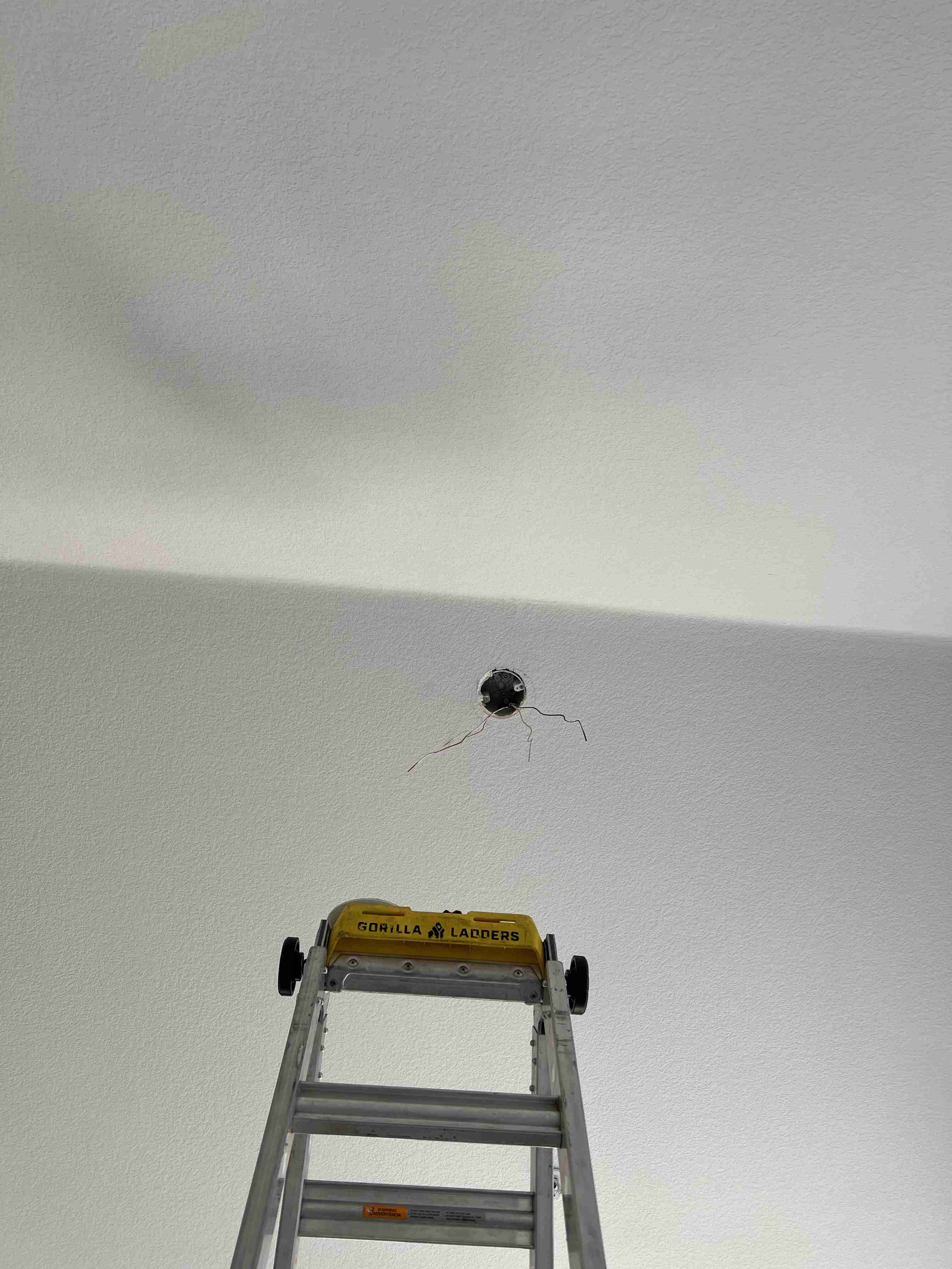 Ladder under hole in ceiling with wires exposed.