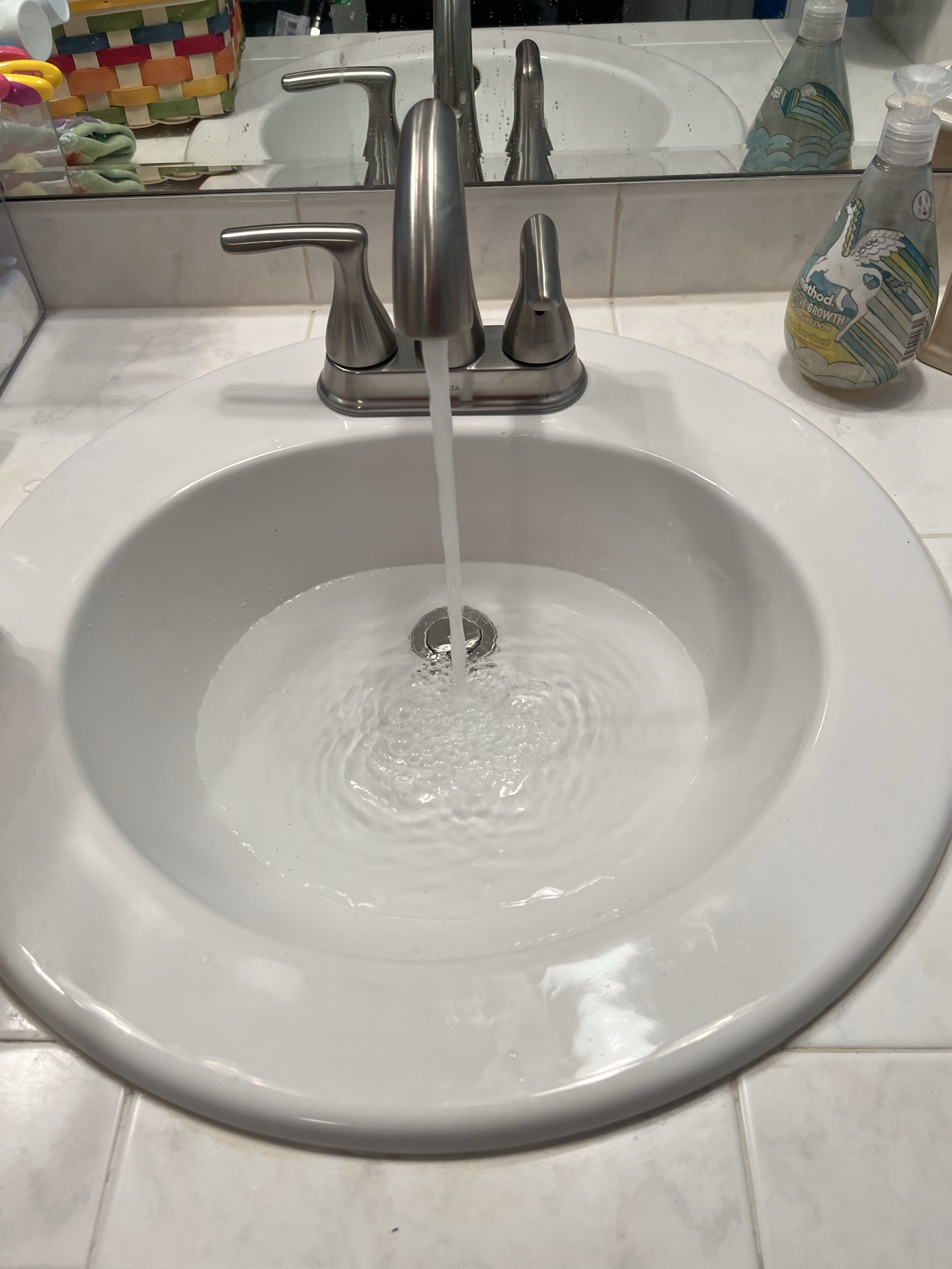 Bathroom sink with running water and cleaning supplies nearby.