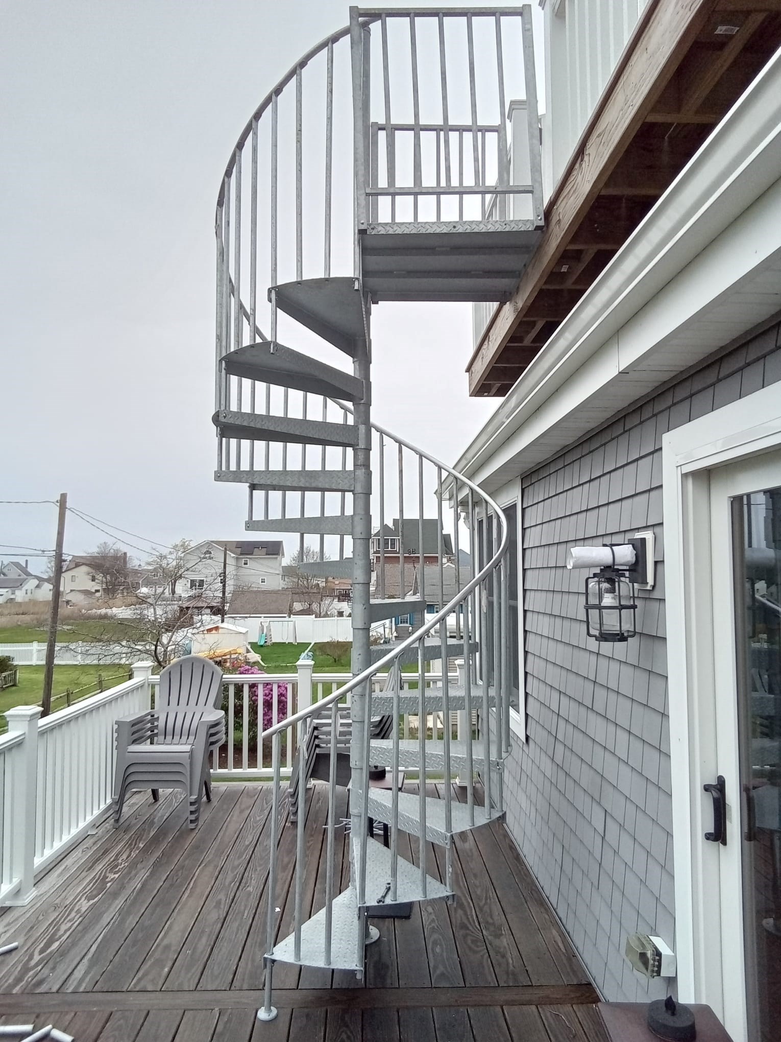 Spiral staircase on a wooden deck leading to an upper balcony.