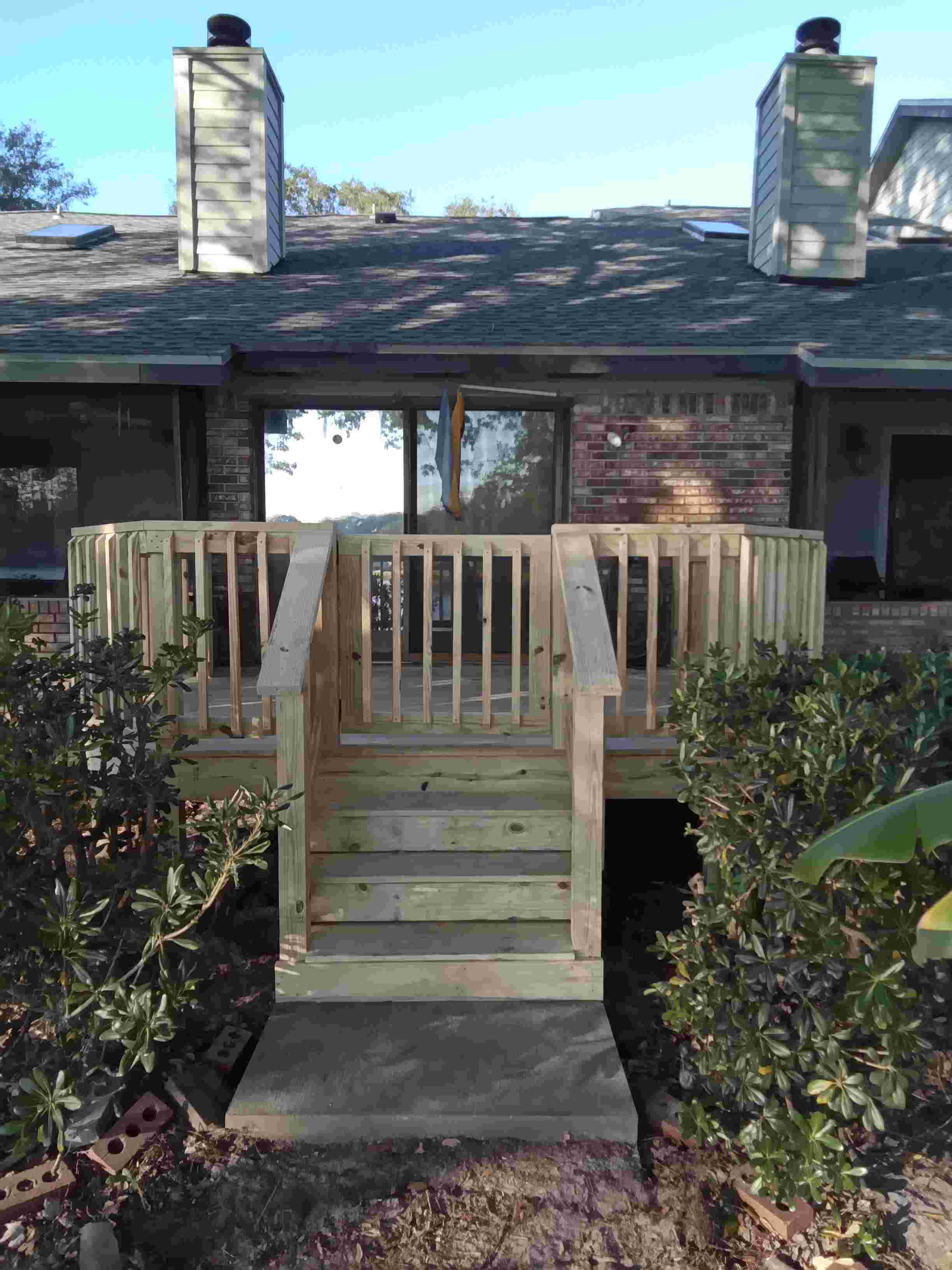 Wooden deck with stairs, surrounded by bushes, in backyard.