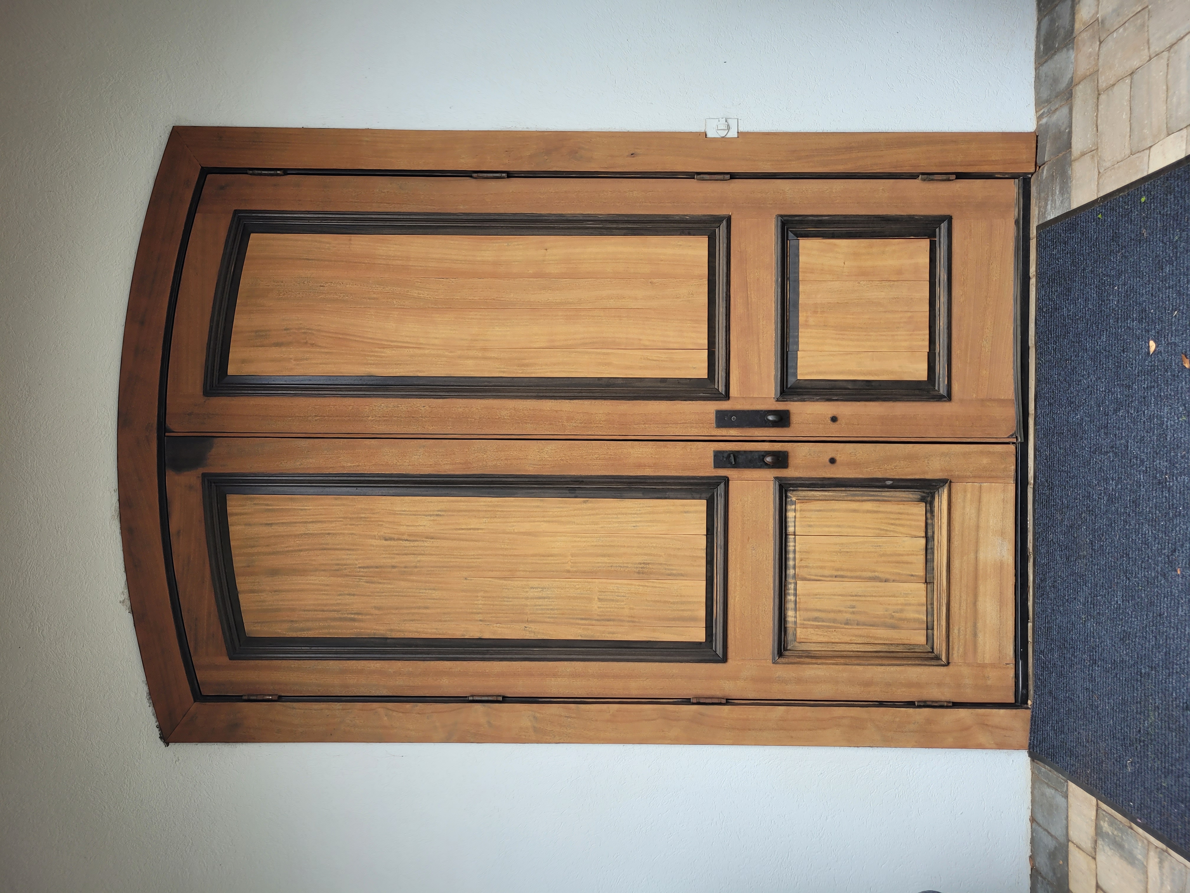Wooden double front door with black trim and arched top.