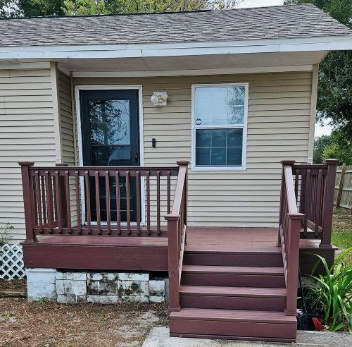 Small porch with brown railing and steps, in need of repair.