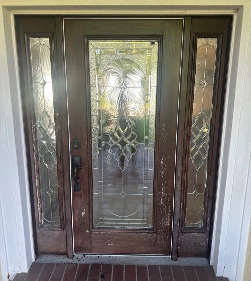 Worn wooden door with ornate glass panels and sidelights.