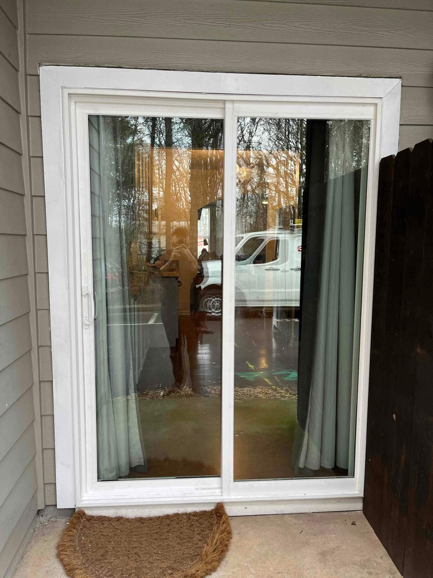Sliding glass door installed with curtains and doormat.
