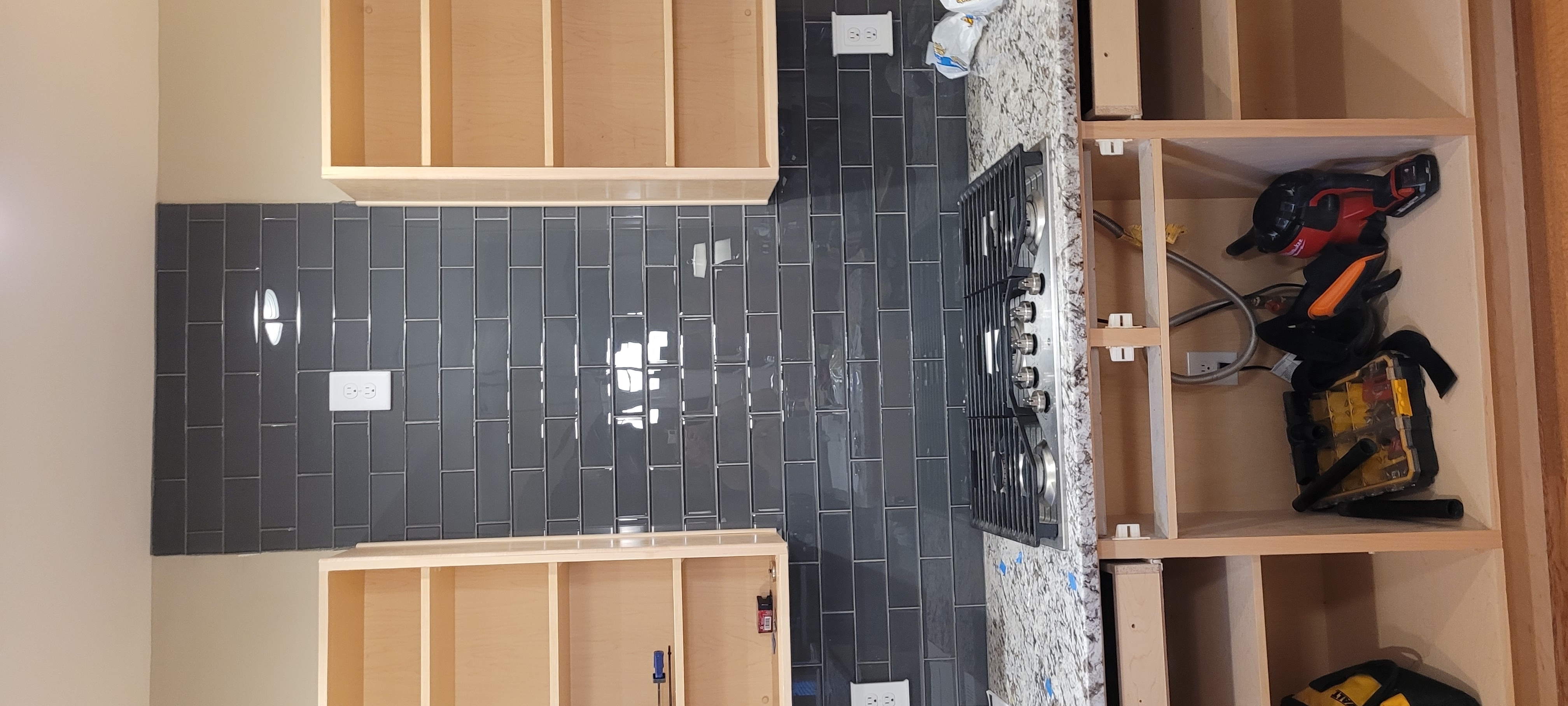 Kitchen backsplash installation with cabinets and tools.