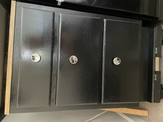 Black three-drawer cabinet with silver knobs on wooden base.