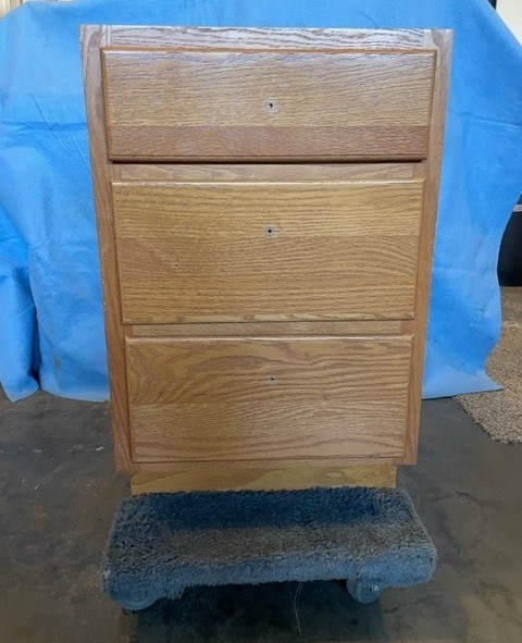 Wooden three-drawer cabinet on a wheeled platform.