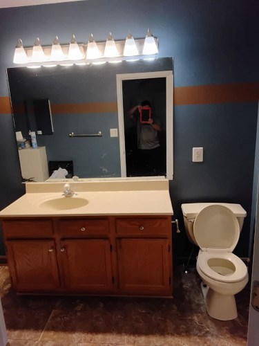 Bathroom renovation with sink, mirror, toilet, and blue walls.