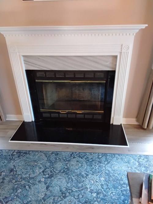 White fireplace with black hearth on a patterned blue carpet.