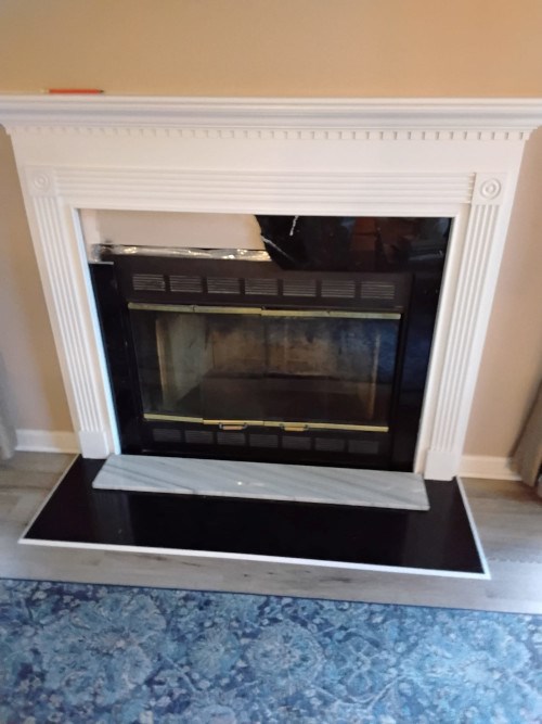 White fireplace with dark glass front, set on black hearth.