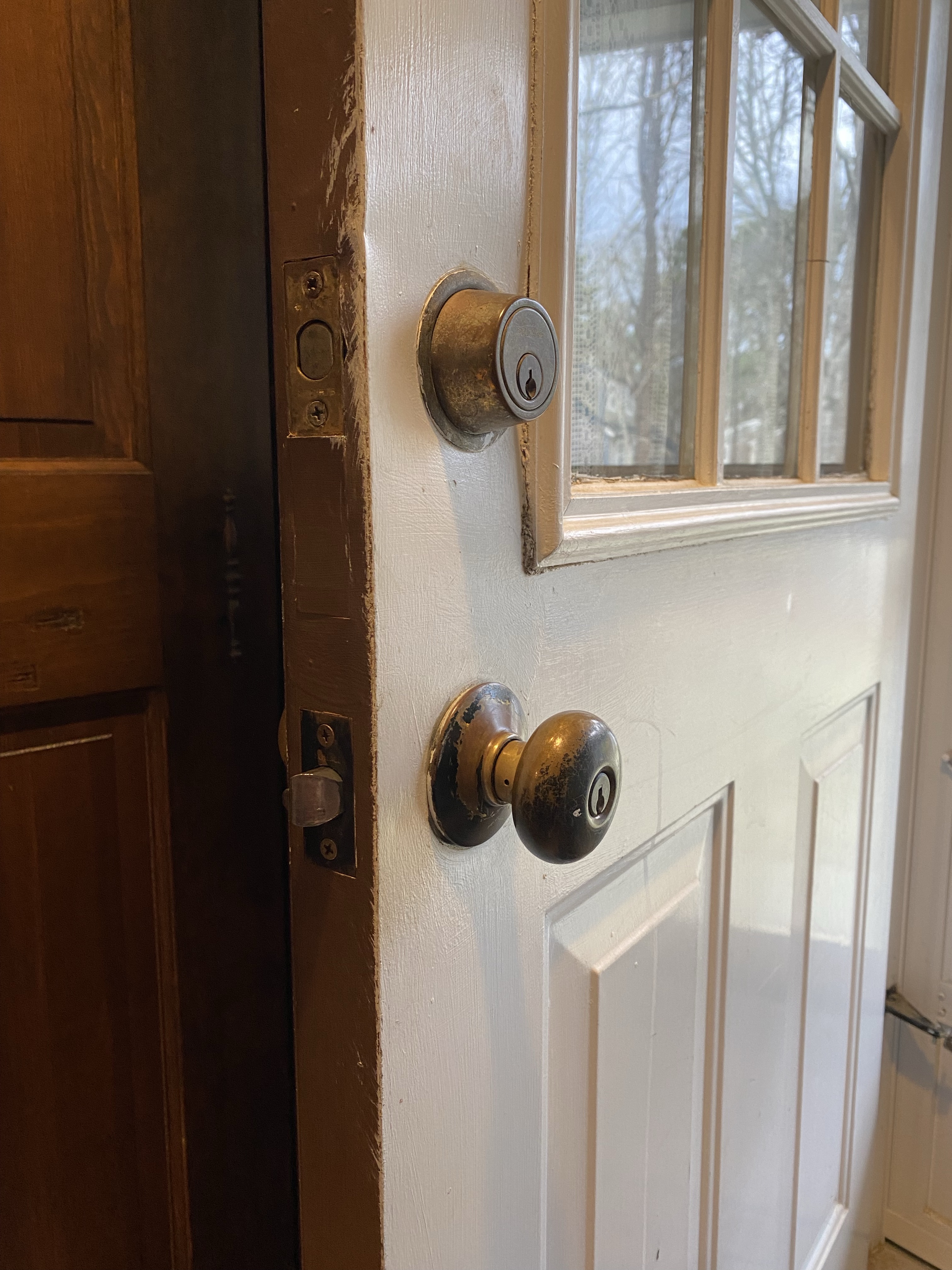 Old white door slightly ajar with worn brass knobs.