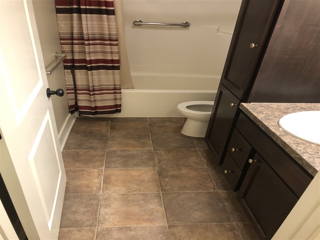 Bathroom with brown cabinets and red-striped shower curtain.