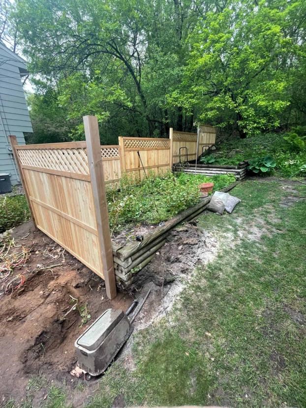 Wooden fence installation near a garden with lush greenery.