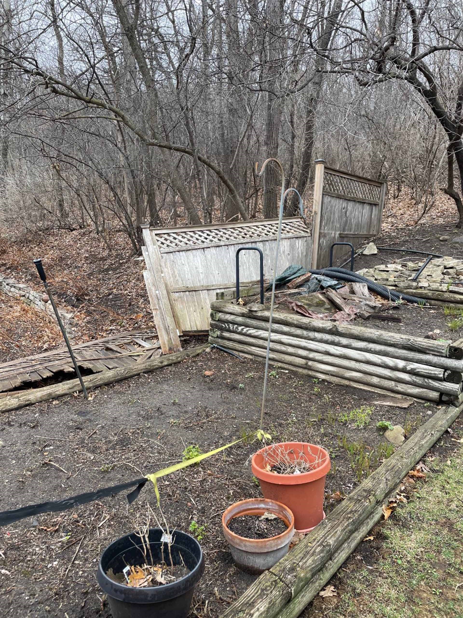 Outdoor garden with fallen fences and potted plants.