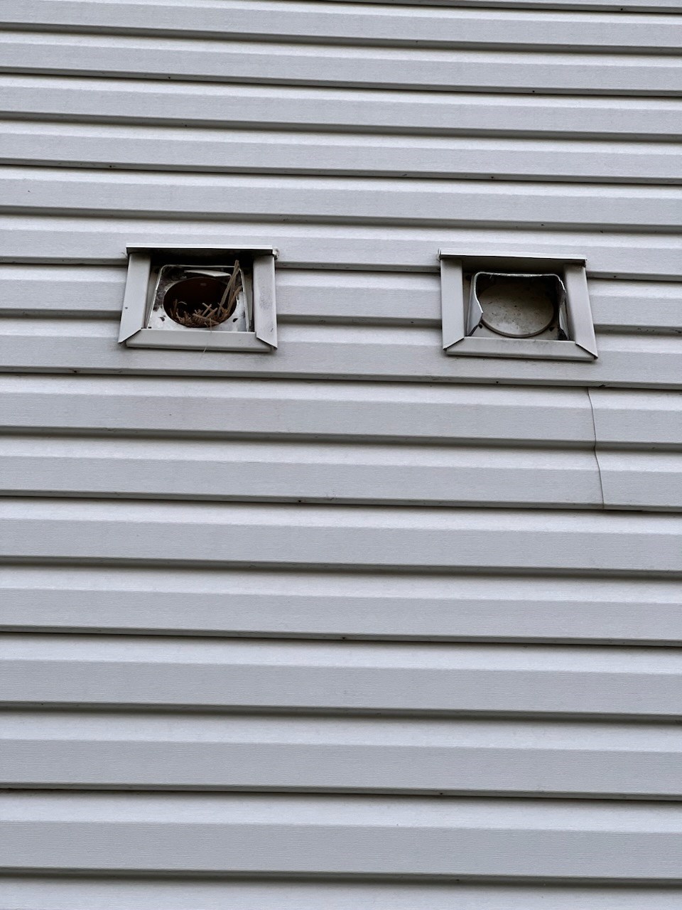 Two square vents on a white siding wall needing repair.
