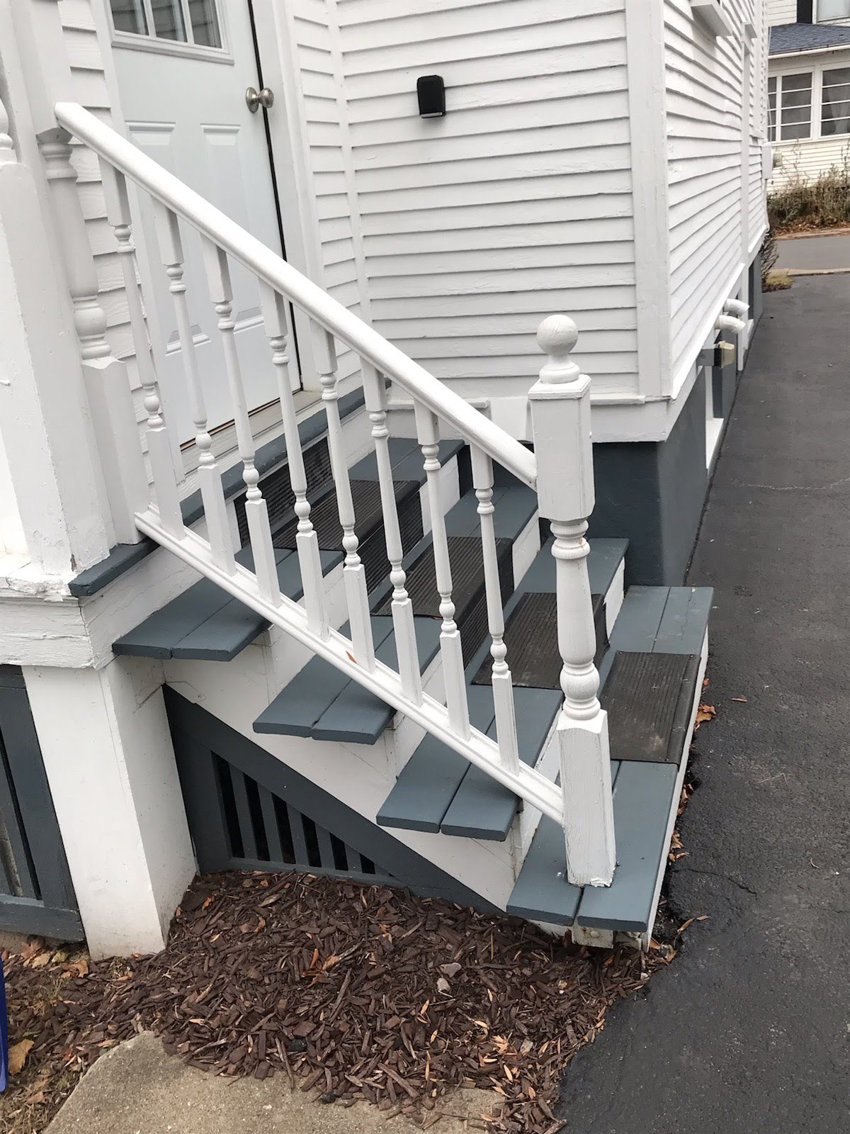 White wooden stairs with railing, leading to a house door.
